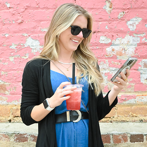 Female F&M Bank client looking at phone and smiling with smoothie in hand