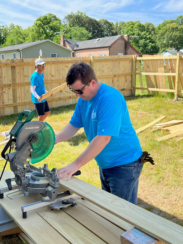 F&M Bank teammate uses a saw to cut wood for a fence that is being built