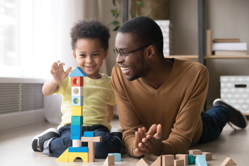 A father and his son playing with toys in their home.