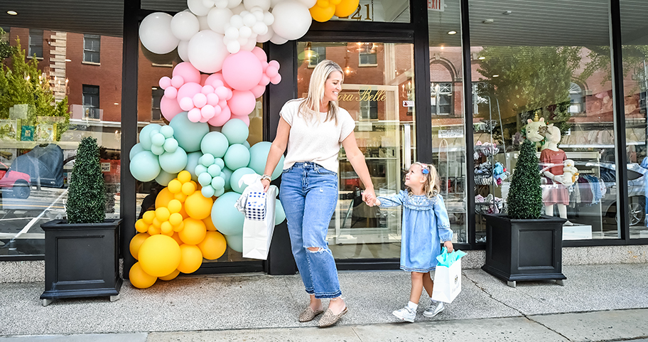 A woman and her daughter holding hands and smiling, while leaving a local shop 