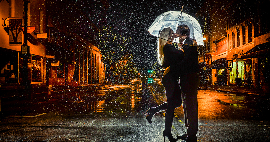 Two people romantically kissing under an umbrella in the rain