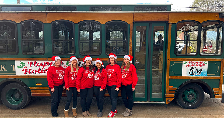F&M Bank employees dressed up for the holidays standing in front of a trolley 
