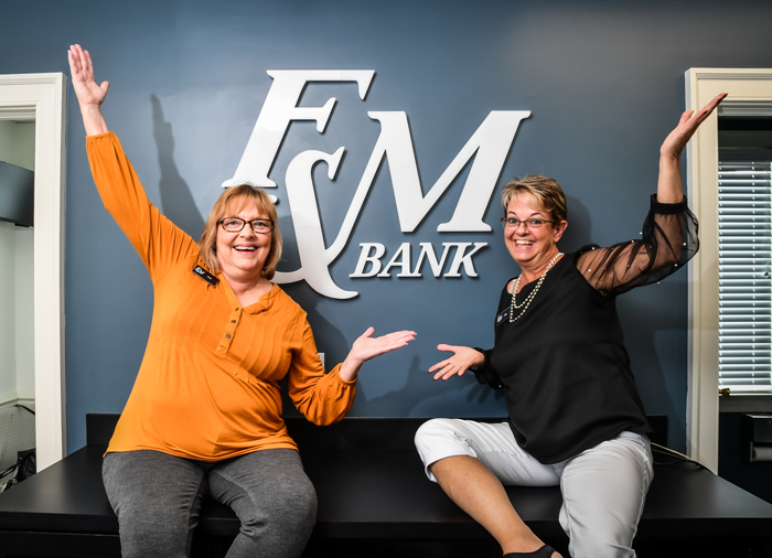 Two employees having fun showing off the F&M Bank logo at the office.